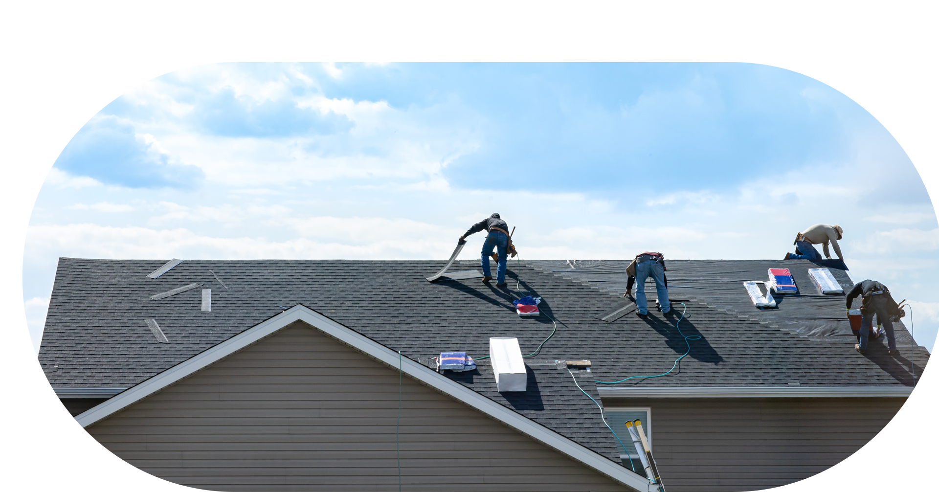 Roofers working on a house roof under a cloudy blue sky.