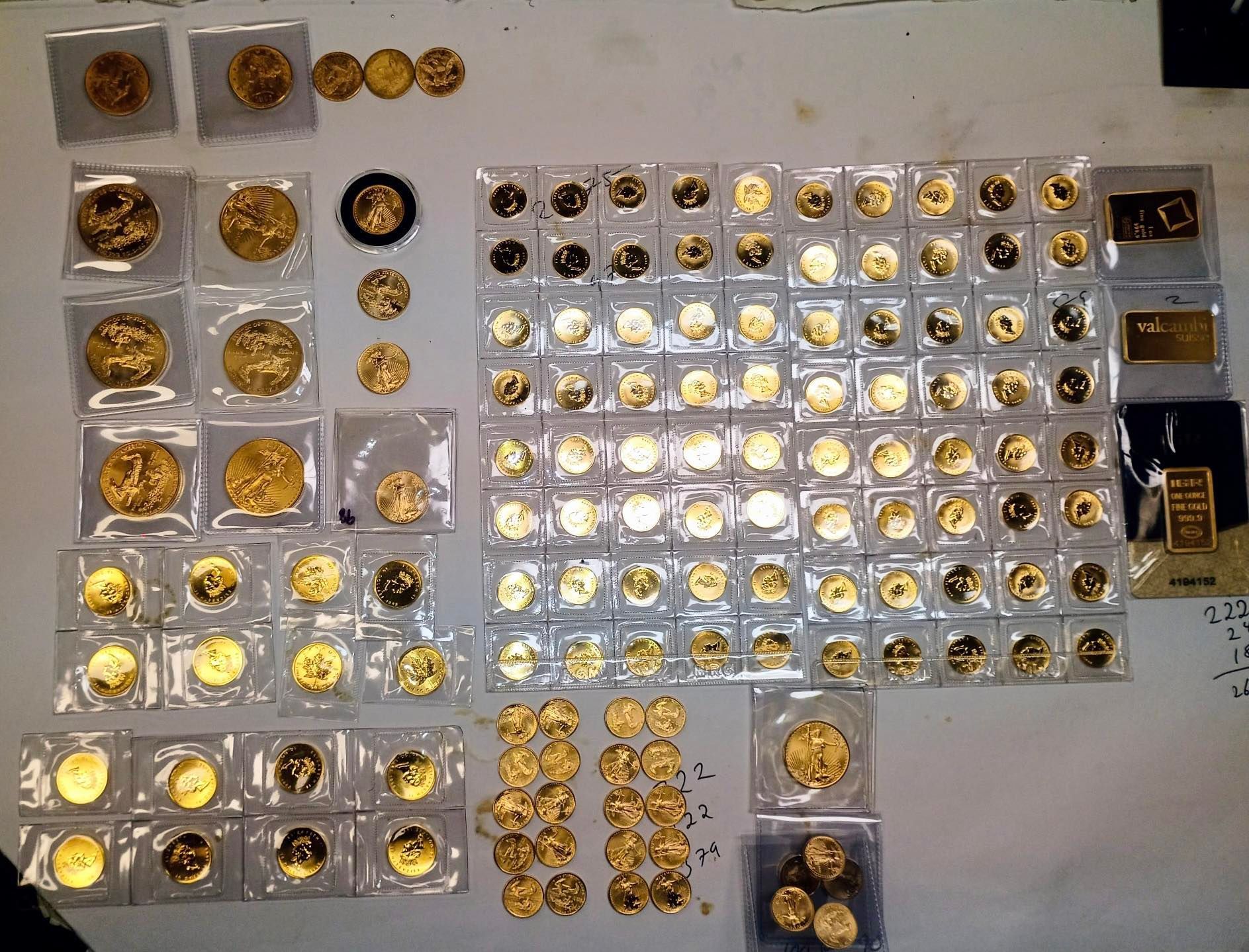 A collection of gold coins and bars displayed on a white surface, neatly organized in plastic cases.