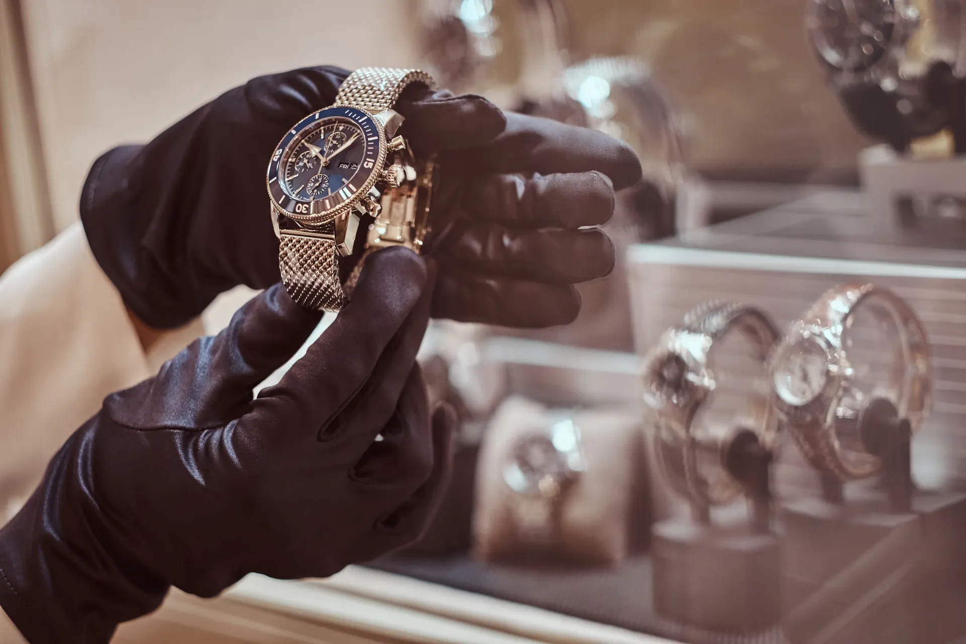 Gloved hands examining a gold wristwatch in a jewelry display case