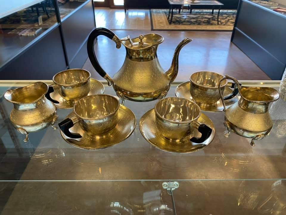 A brass tea set is sitting on a glass table.