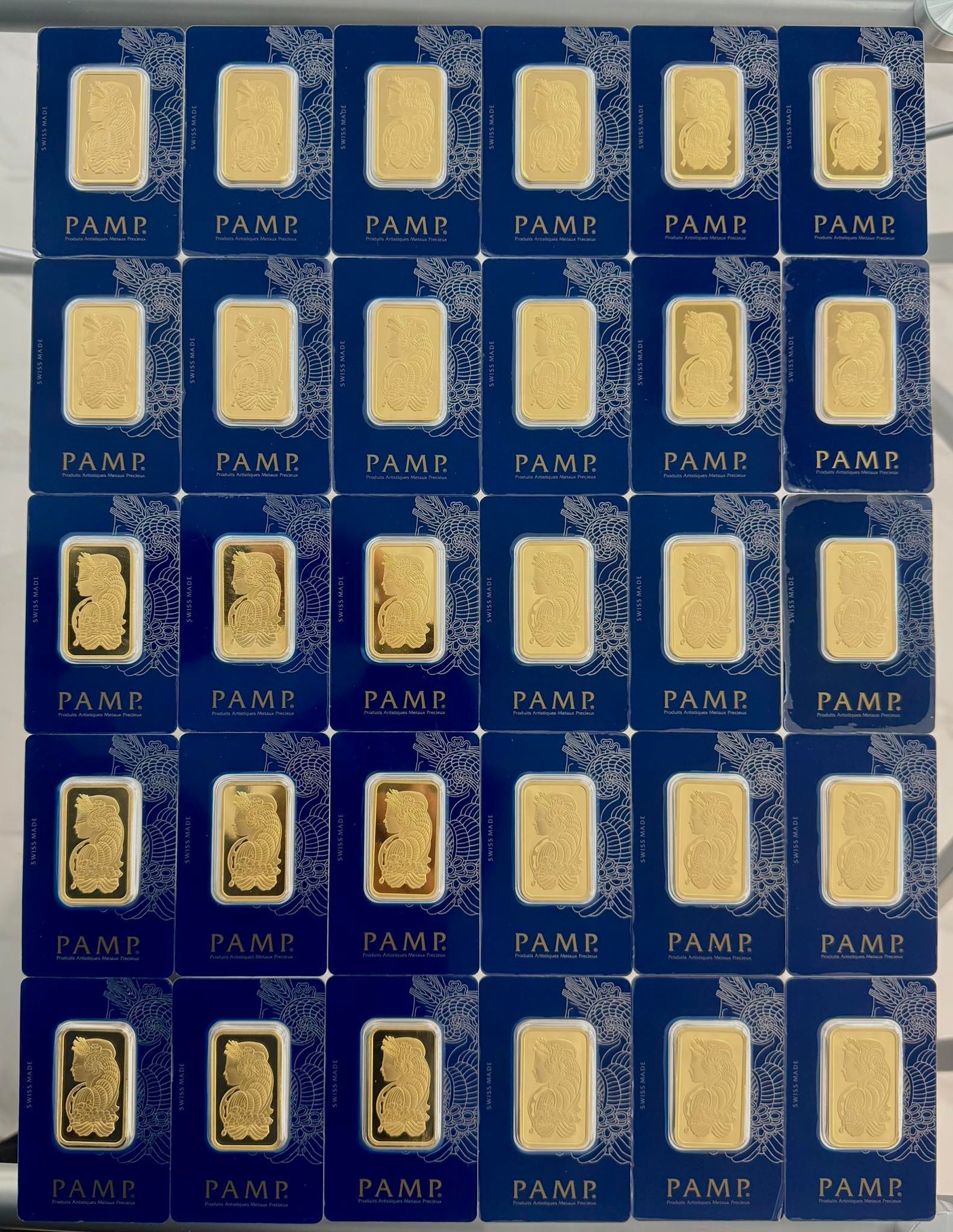 Arrangement of 30 gold bars, each in a blue protective card with decorative borders, arranged on a surface.