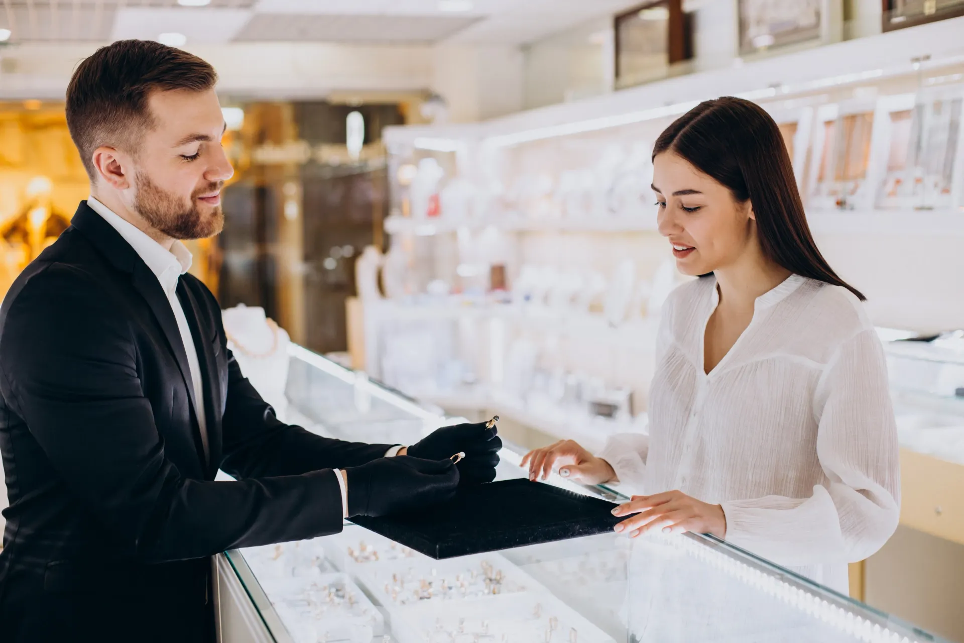 Sales associate shows black fabric to a customer at a jewelry counter in a bright store