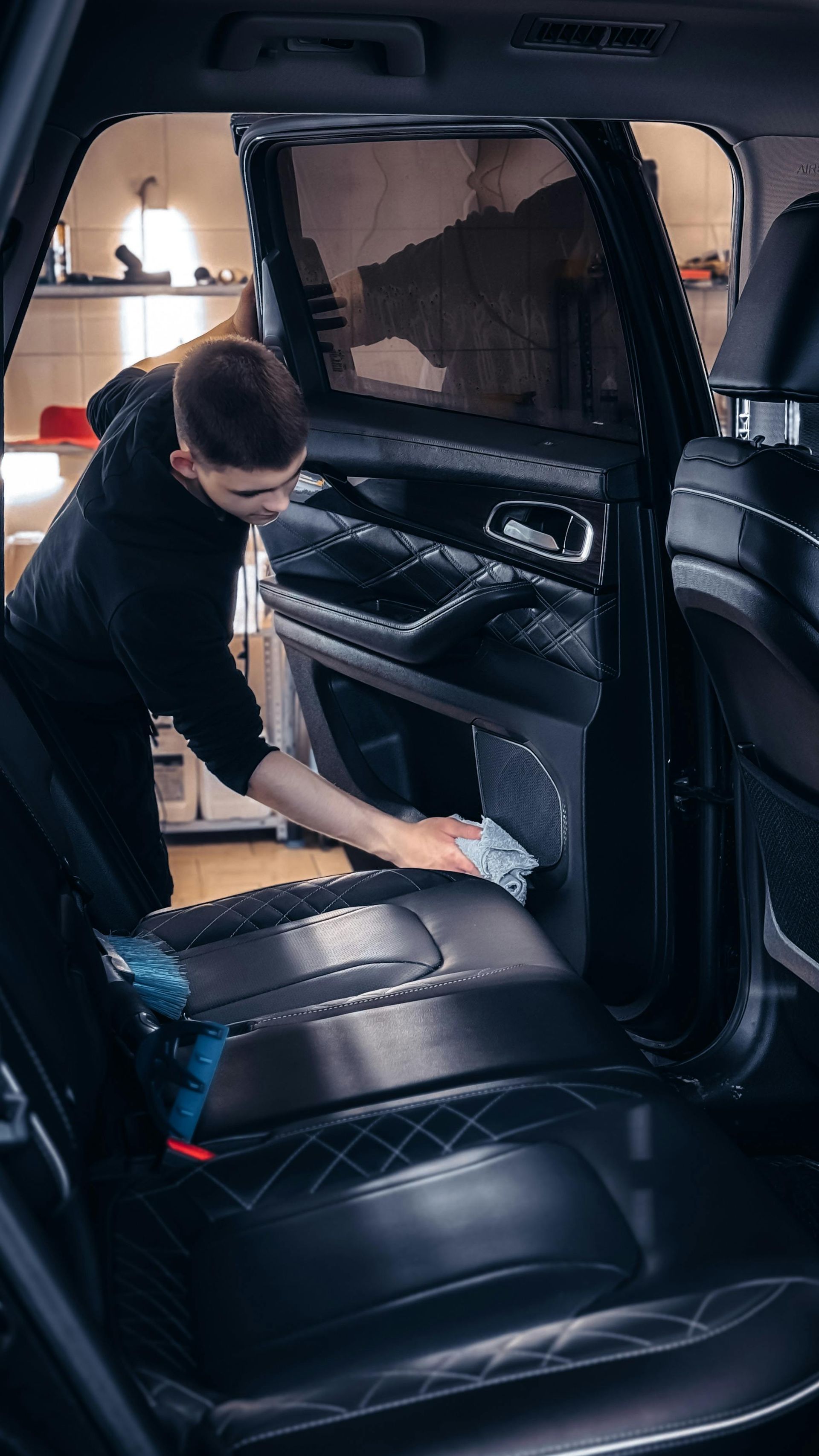 Man cleaning the interior of a black car with a cloth in a garage.