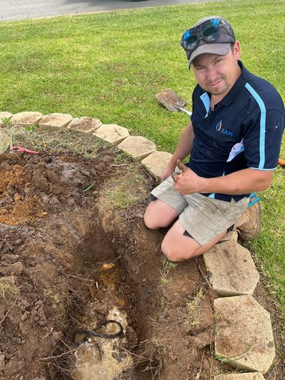 A Man is Kneeling in the Dirt in a Garden — Wello's Plumbing & Gas In Thurgoona, NSW