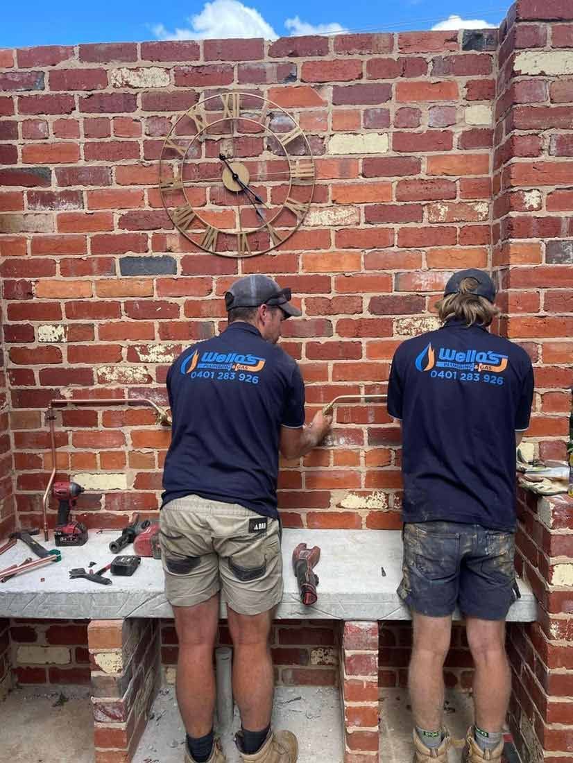Two Men Are Working on a Brick Wall — Wello's Plumbing & Gas In Thurgoona, NSW
