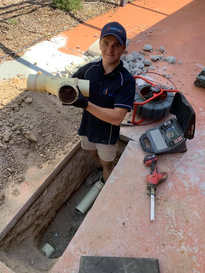 A Man Is Standing In A Hole In the Ground Holding A Pipe  — Wello's Plumbing & Gas In Thurgoona, NSW