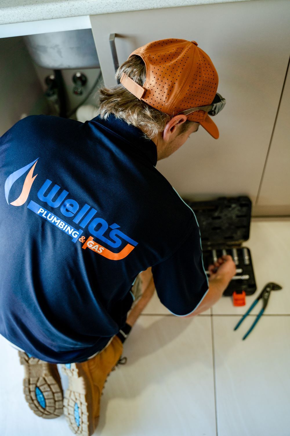 A Man in A Blue Shirt Is Working on A Sink — Wello's Plumbing & Gas in Thurgoona, NSW