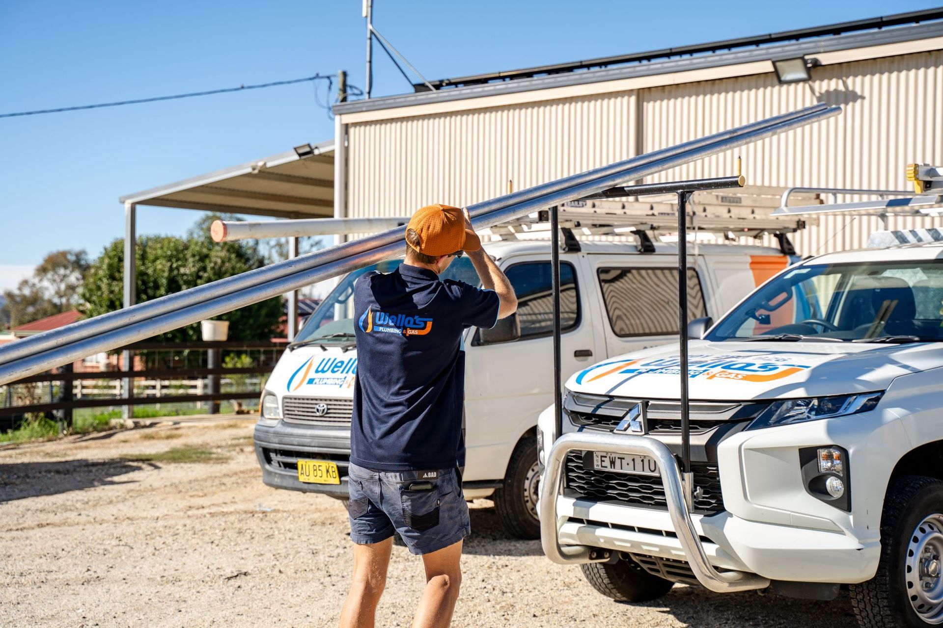 A Man Is Carrying A Large Steel Pipe — Wello's Plumbing & Gas In Thurgoona, NSW