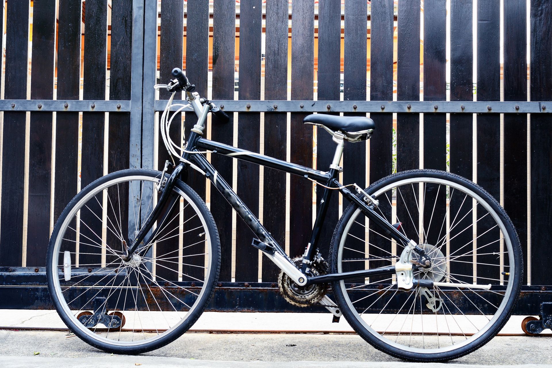 A black mountain bike parked sideways against a dark wooden gate.