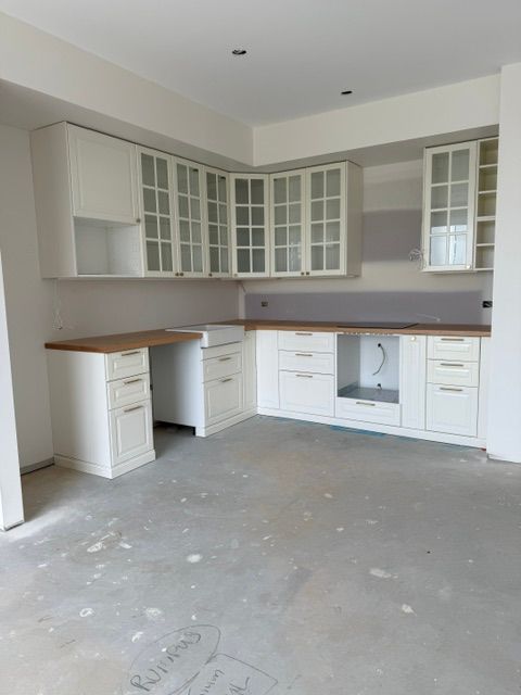 Empty white kitchen under renovation with unfinished concrete floor and wood countertops