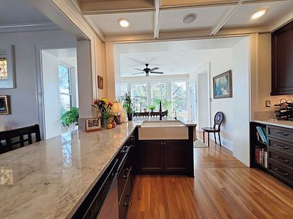 Bright modern kitchen with marble island, wood floors, and view into sunlit dining area.
