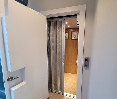Open elevator door with metal folding gate in a hallway, wood-paneled interior visible inside.