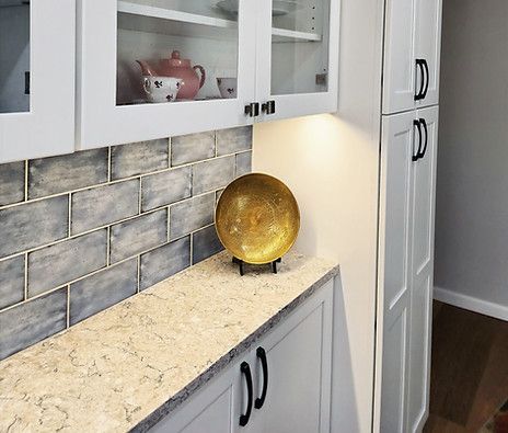 Modern kitchen with white cabinets, gray tile backsplash, and a gold decorative bowl on a beige countertop.