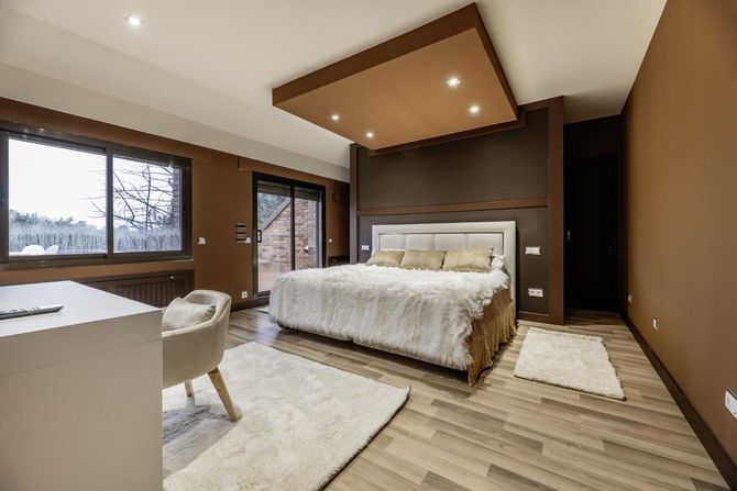 Modern bedroom with a large bed, wood-paneled walls, windows, and a desk chair