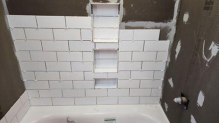 Partially tiled shower wall under renovation with white subway tiles and exposed brown wall edges
