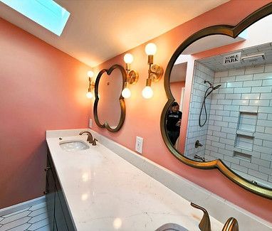Pink bathroom with long white vanity, round mirrors, and wall sconces reflected in the mirror