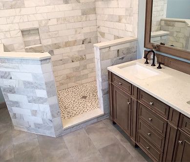 Walk-in shower with marble tile, pebble floor, and adjacent vanity with sink and mirror
