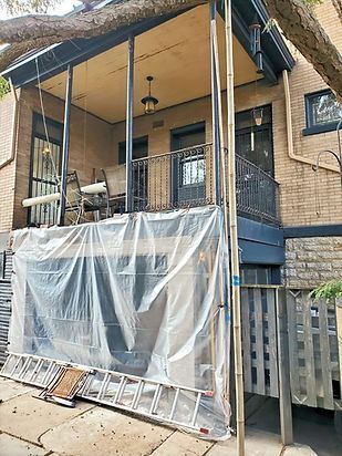 Front porch under renovation, covered in plastic sheeting with scaffolding and a ladder leaning nearby.
