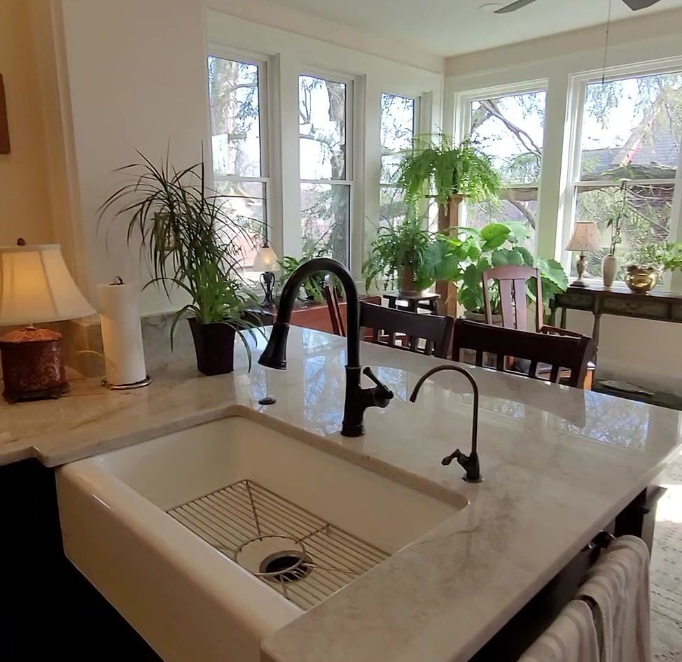 Bright kitchen with white island sink, black faucet, and large windows overlooking potted plants