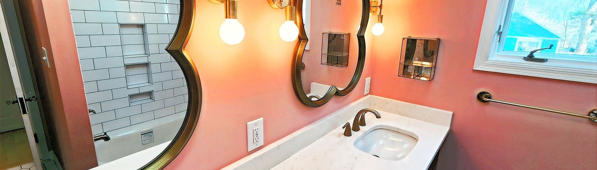 Pink bathroom with vanity sink, round mirror, lights, and tiled walls