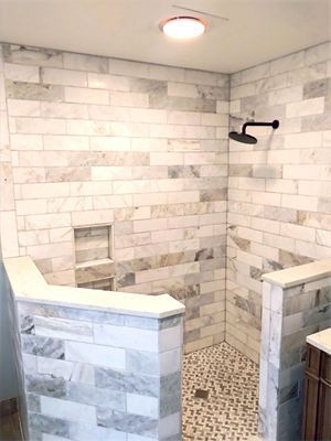 Walk-in shower with white marble tile, mosaic floor, and a ceiling light