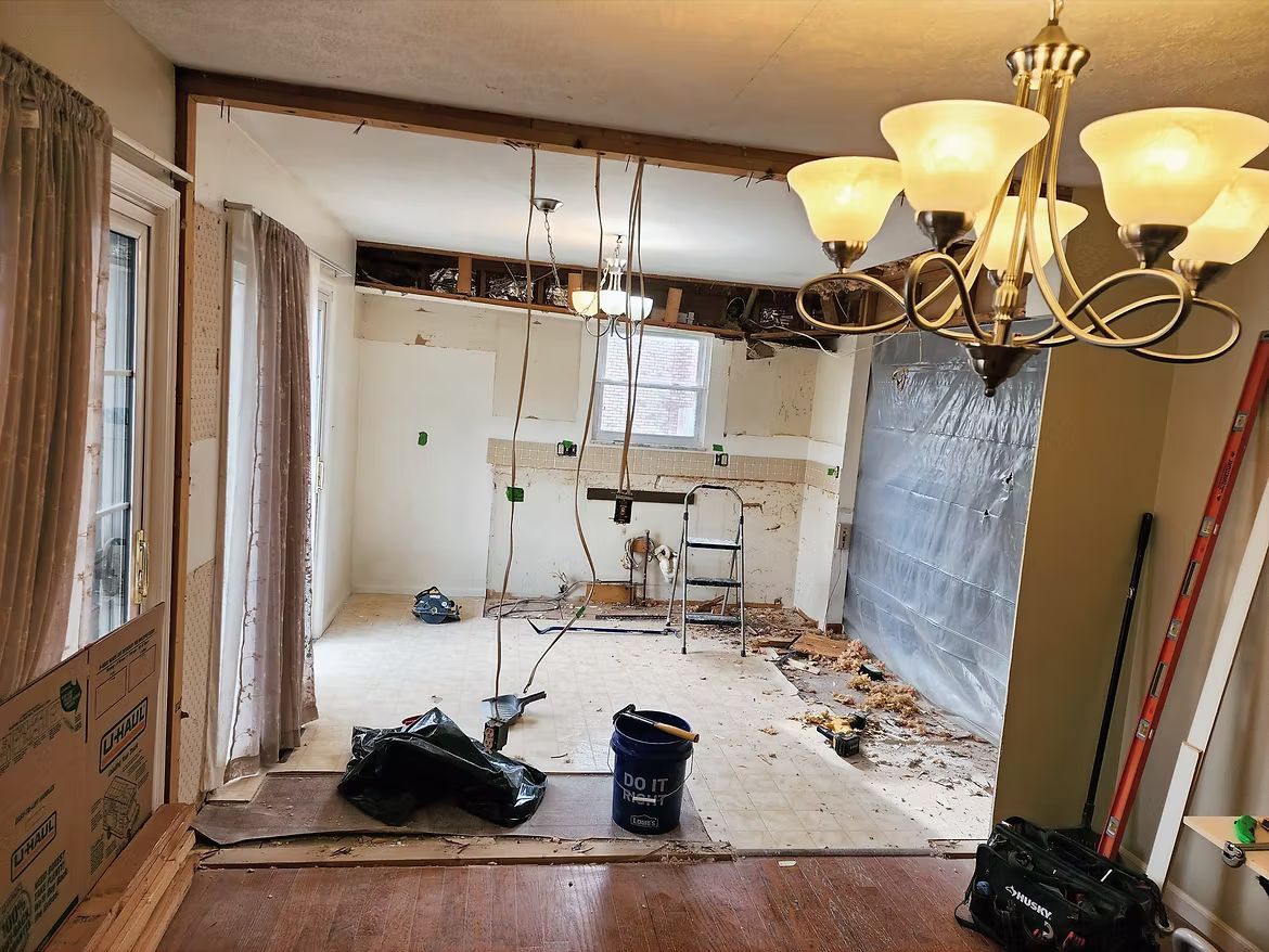 Partially demolished kitchen and dining room with debris, exposed walls, and hanging chandelier