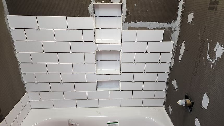 Bathroom shower wall under renovation with white subway tile and gray drywall around it