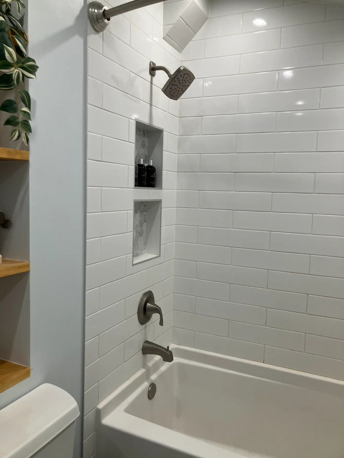 White tiled bathroom shower with built-in shelf and chrome showerhead above a bathtub.