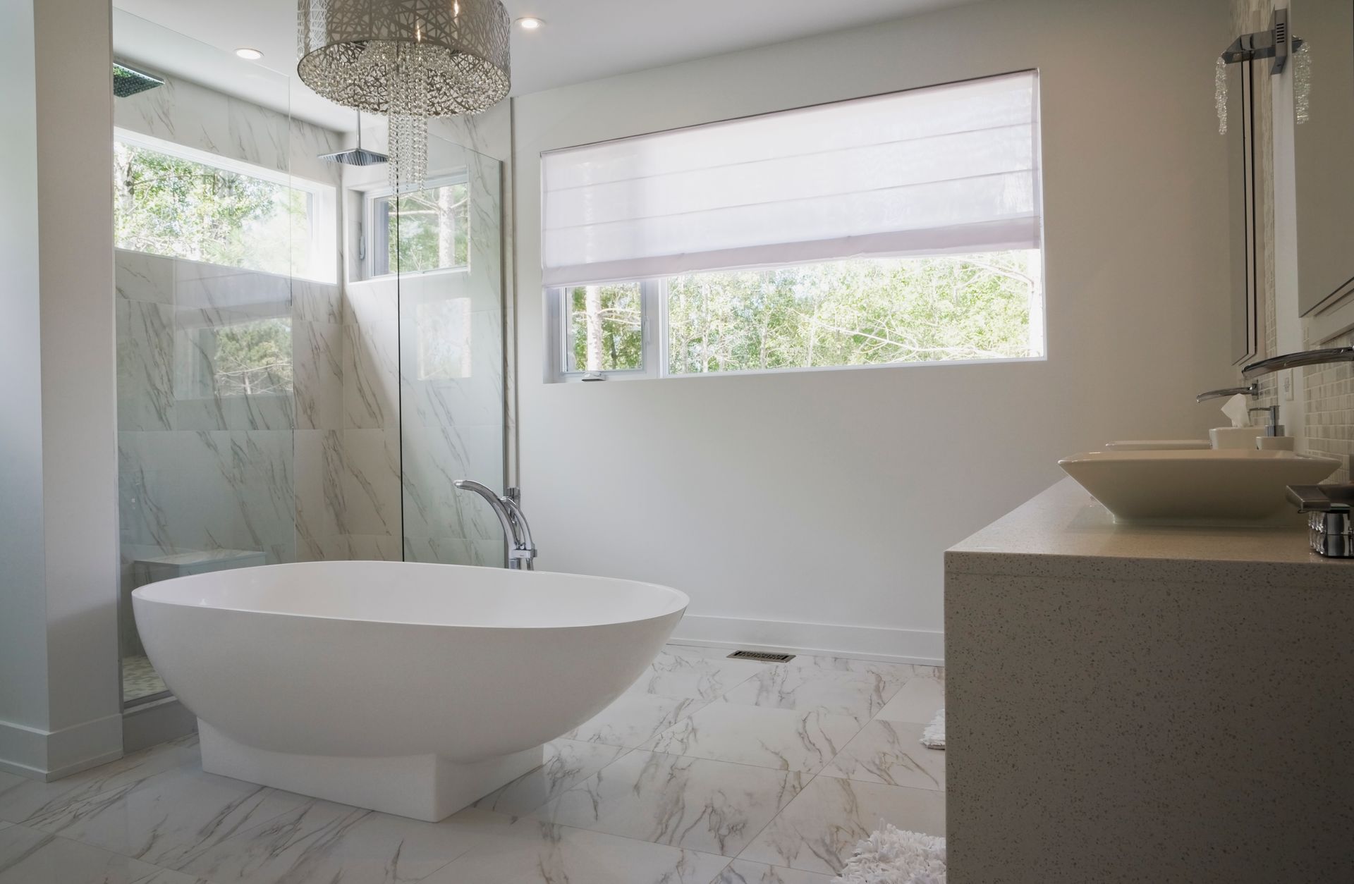 Modern white bathroom with freestanding tub, glass shower, marble floors, and large window