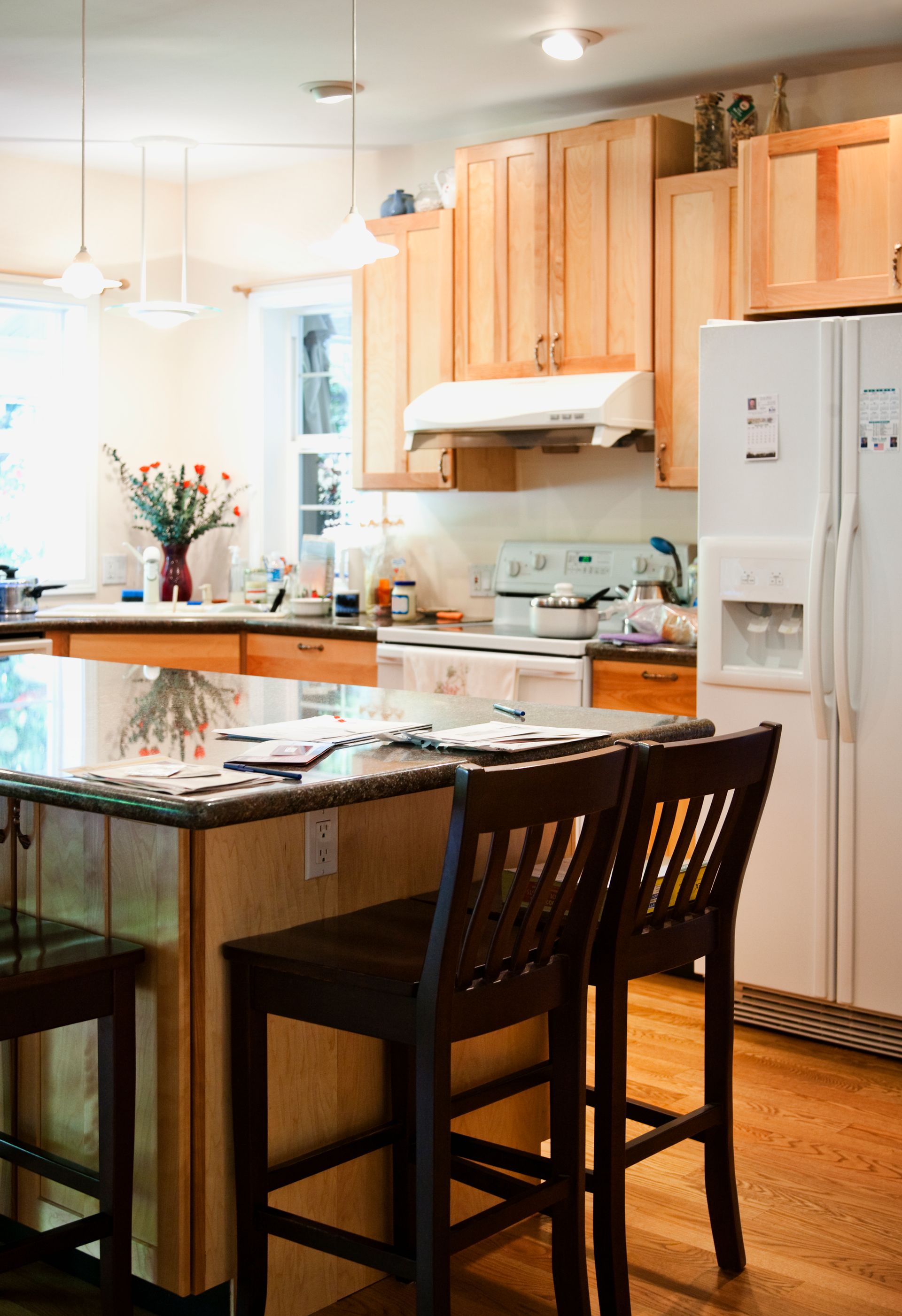 Bright kitchen with wooden cabinets, white appliances, and a granite island with two bar stools