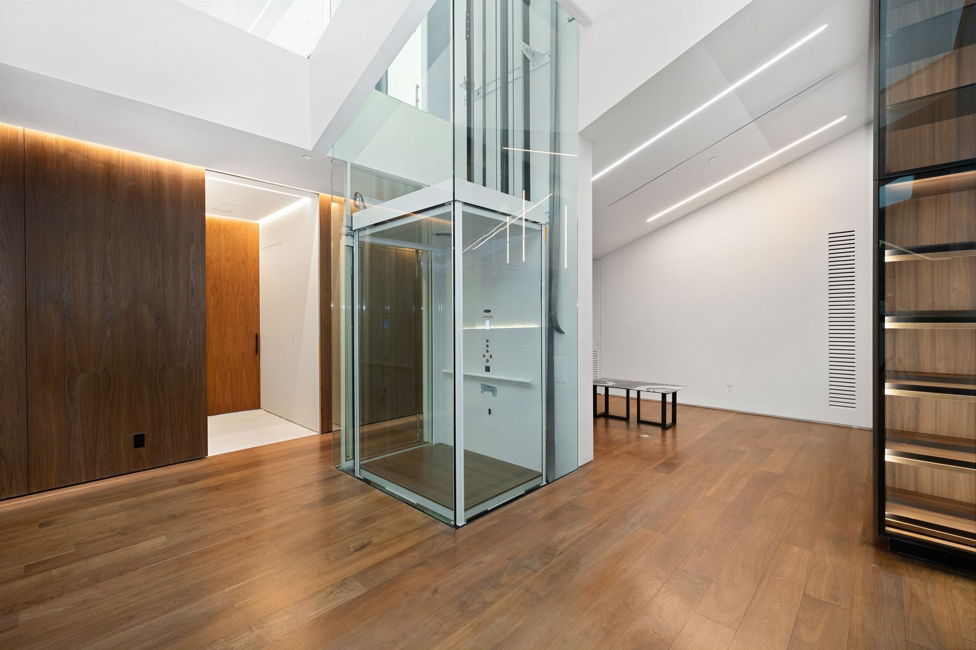 Modern office lobby with wood floors, glass elevator, and white walls