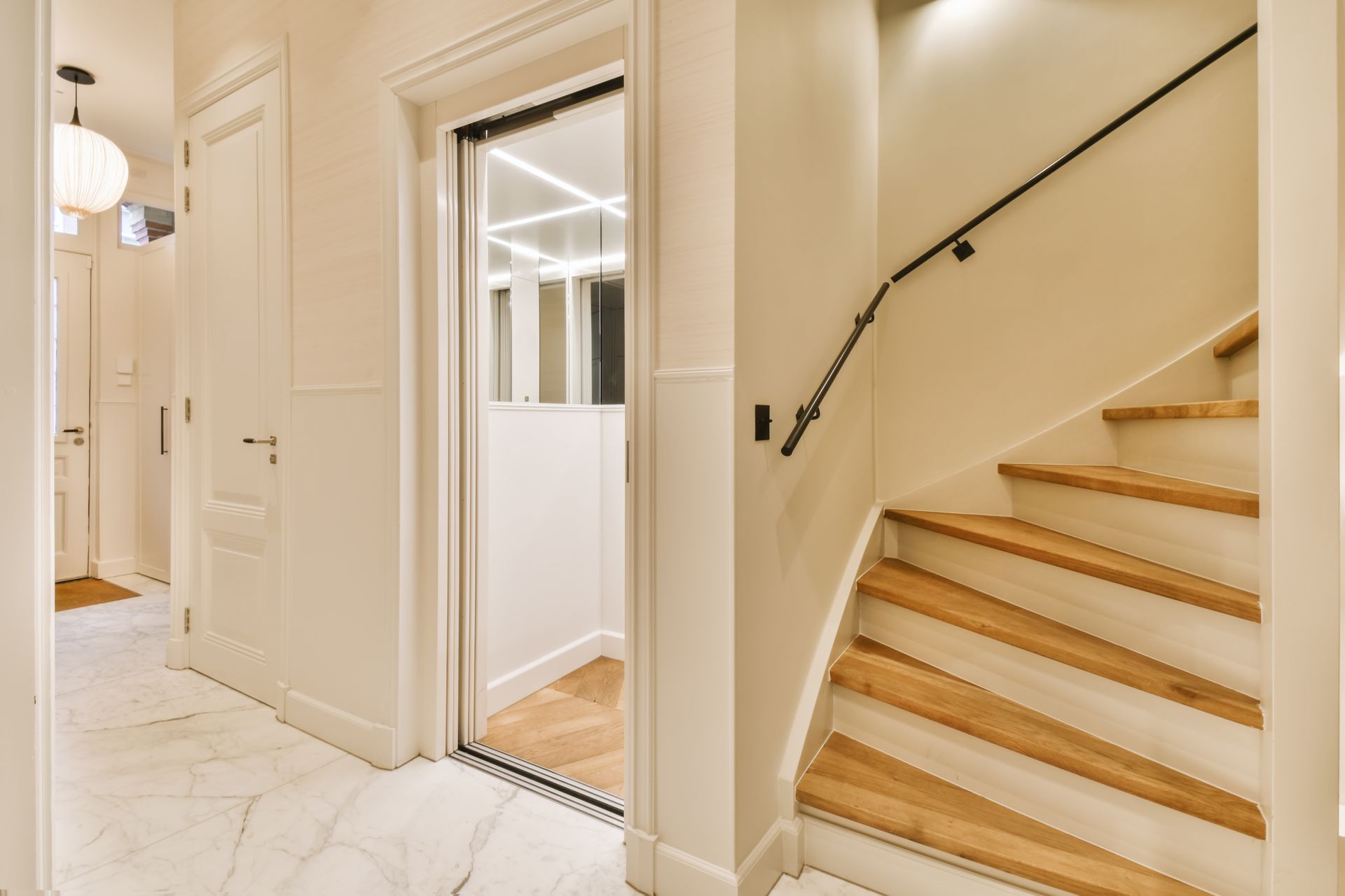 Bright hallway with white marble floor, glass door, and a staircase with light wood steps and black handrail