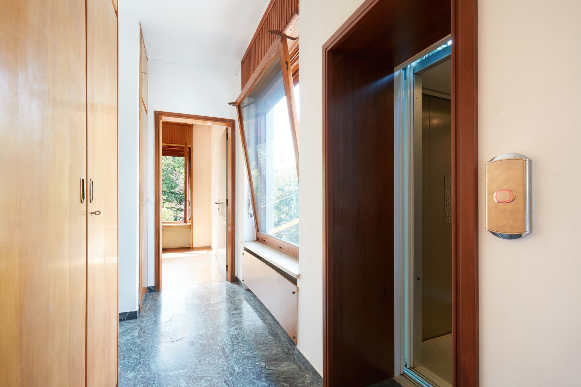 Narrow hallway with wood-paneled walls, elevator on the right, and daylight from a window ahead