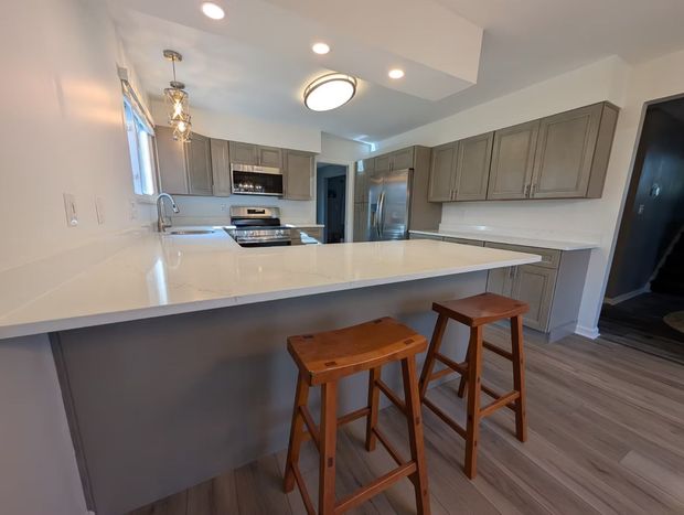 Modern kitchen with white countertops, gray cabinets, and two wooden stools at the island