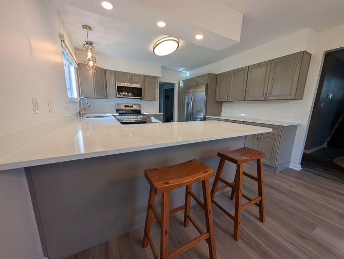 Modern kitchen with white counters, gray cabinets, and two wooden stools at a breakfast bar