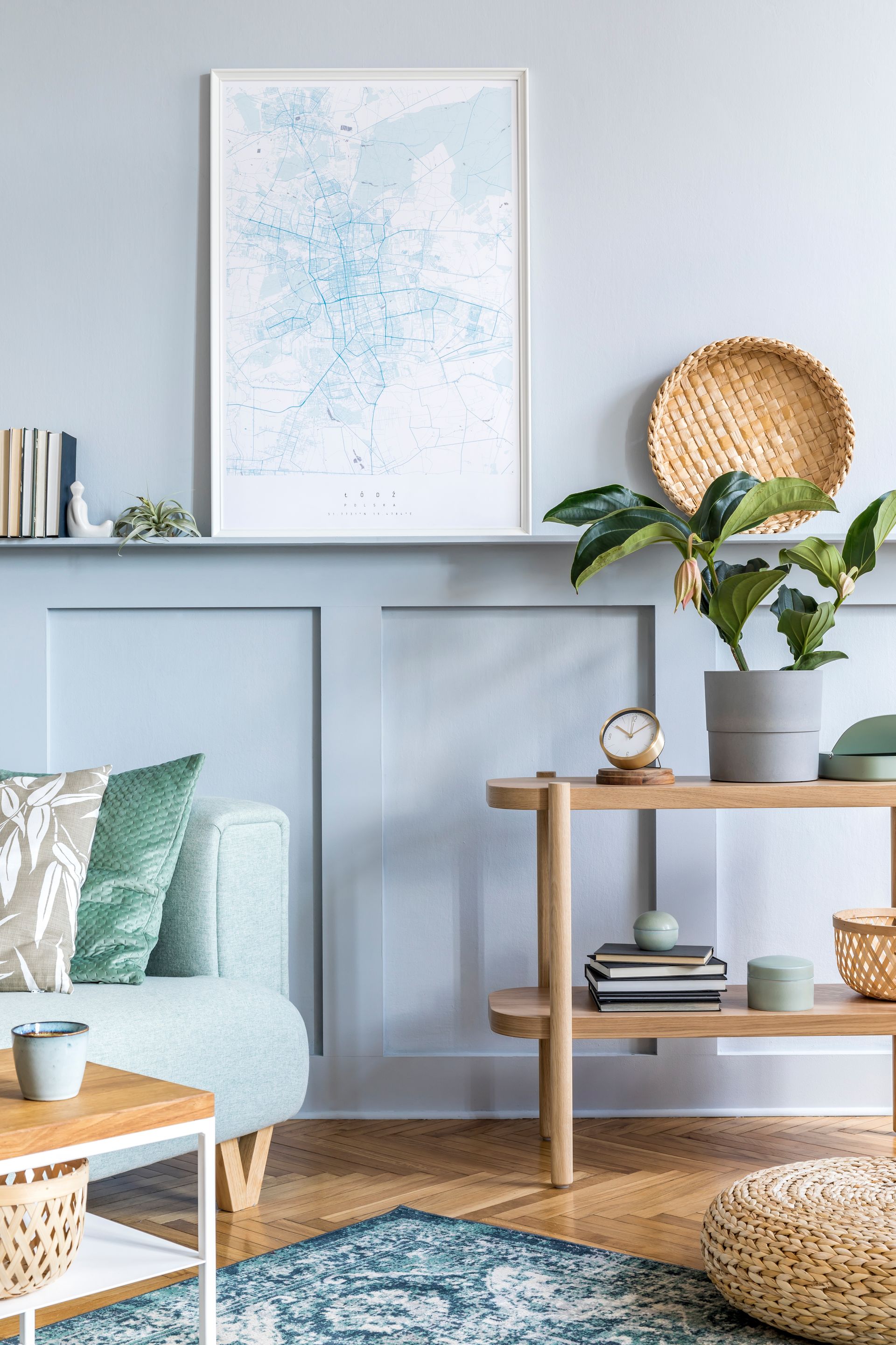 Bright living room with pale blue walls, framed art, woven decor, and a small wooden shelf with plants and books