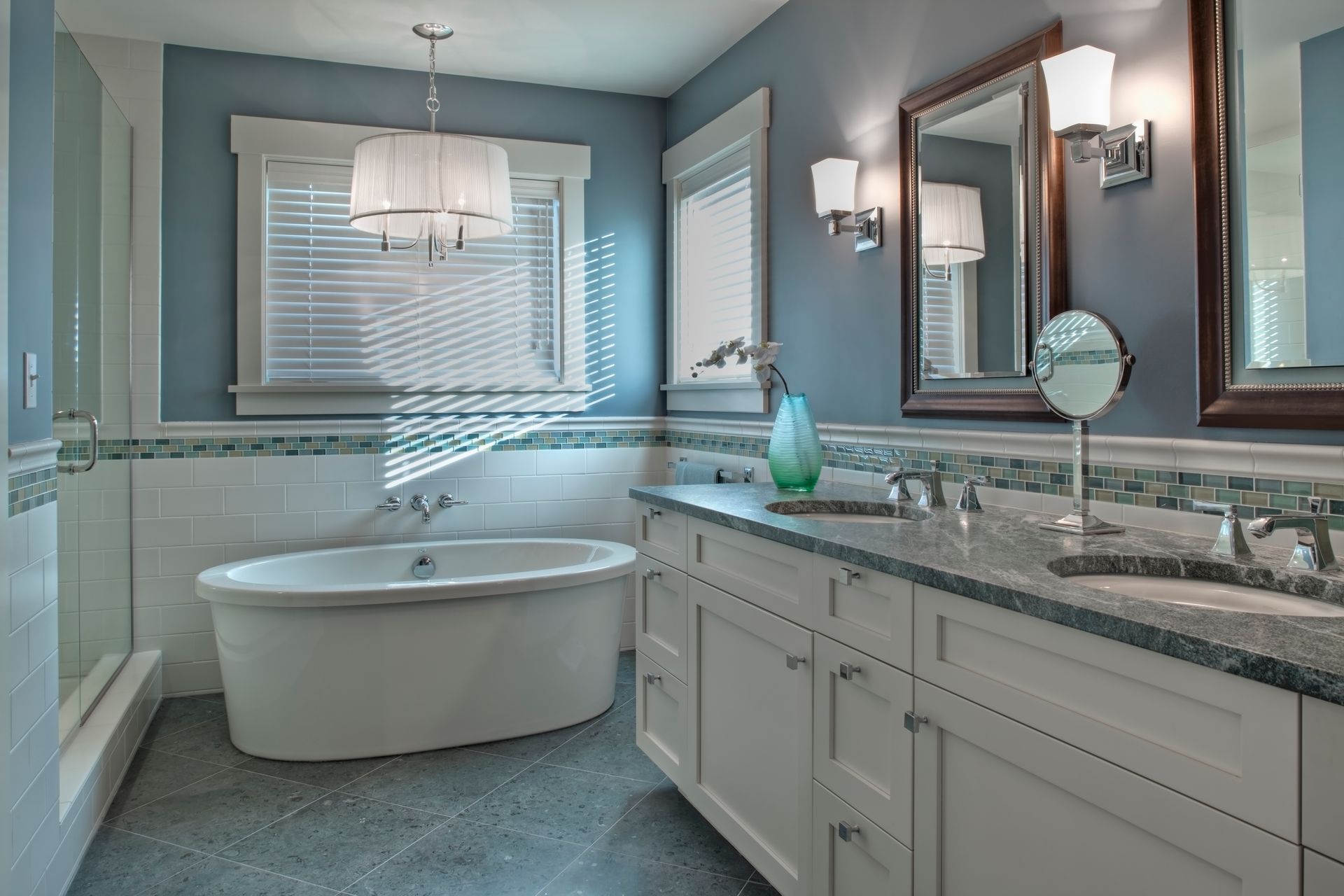 Modern bathroom with freestanding tub, double vanity, mirrors, and soft blue-gray walls