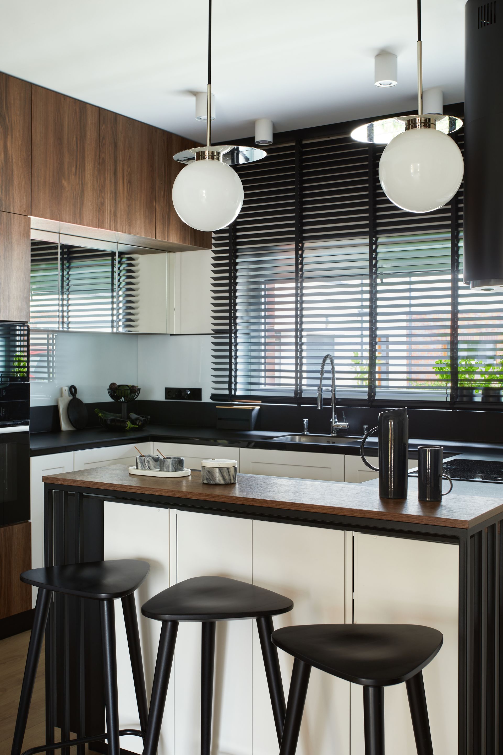 Modern kitchen with island, black stools, pendant lights, and large windows with blinds