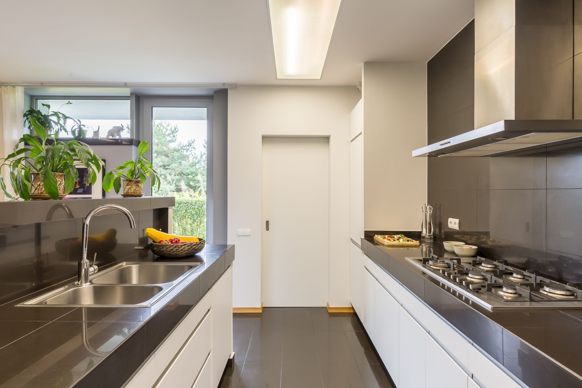 Modern kitchen with a sink, stove, white cabinets, and a window filled with potted plants