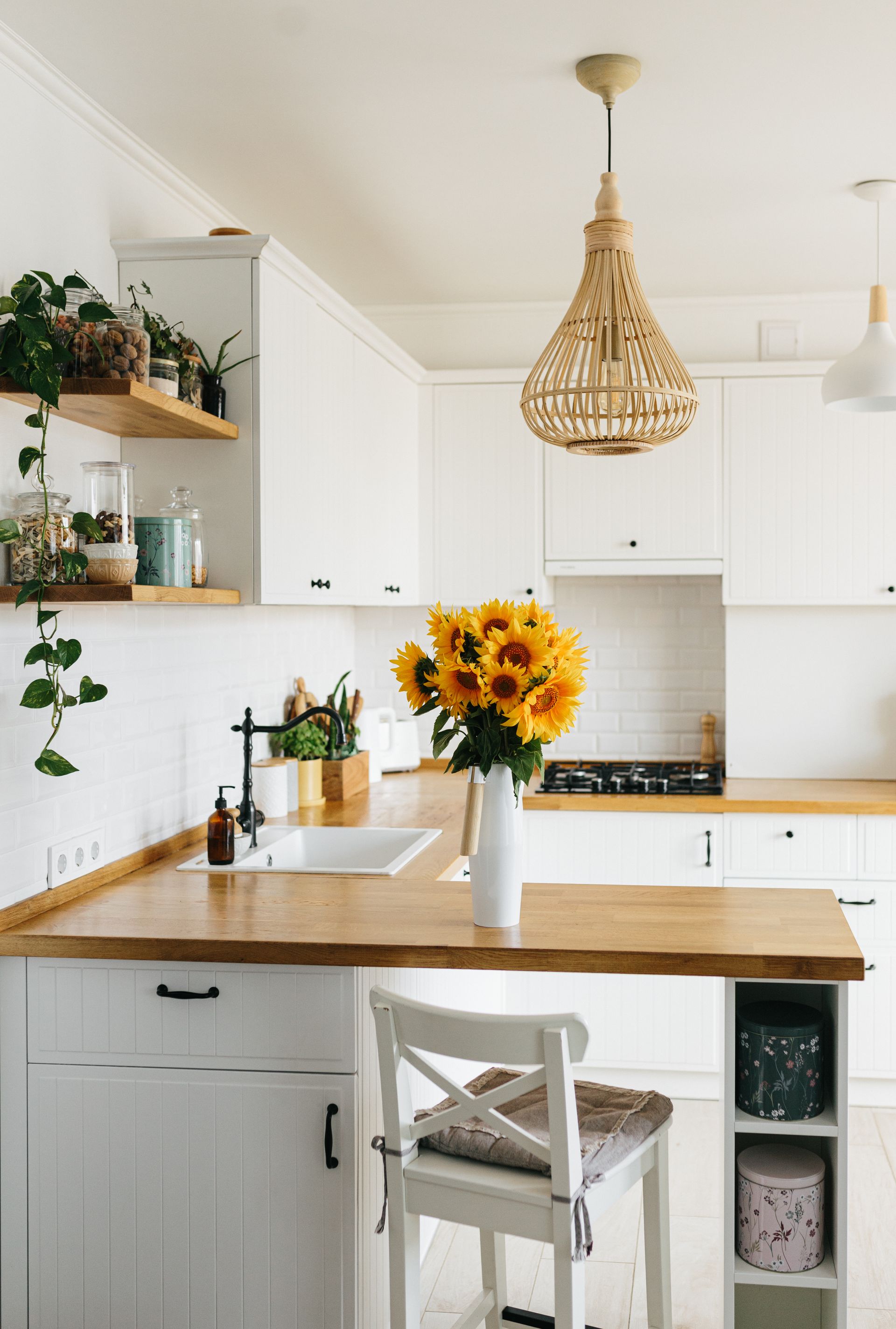 Bright white kitchen with wood countertops, hanging wicker pendant, and sunflowers on the island