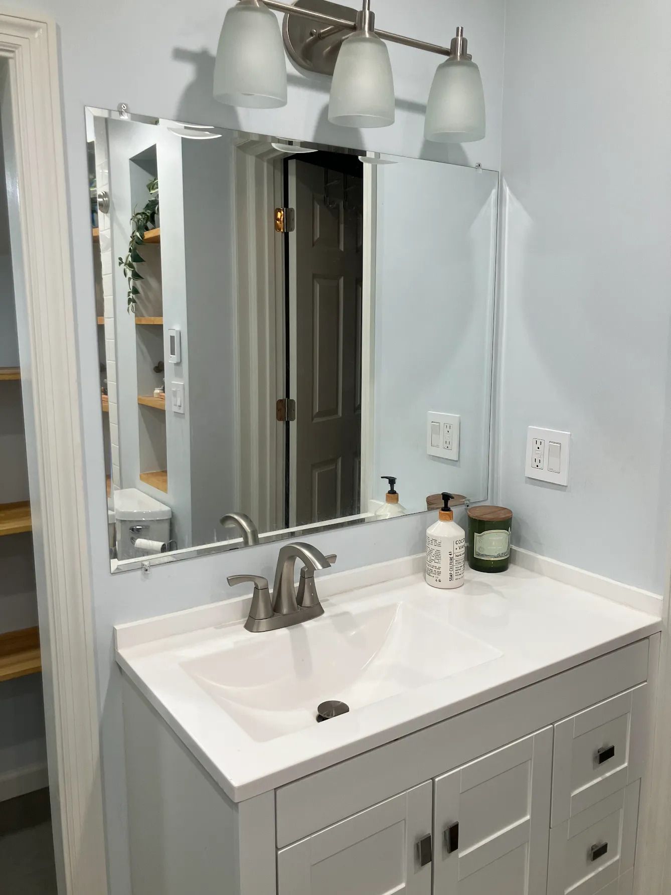 Bathroom vanity with white sink, gray cabinet, mirror, and three light fixtures above it