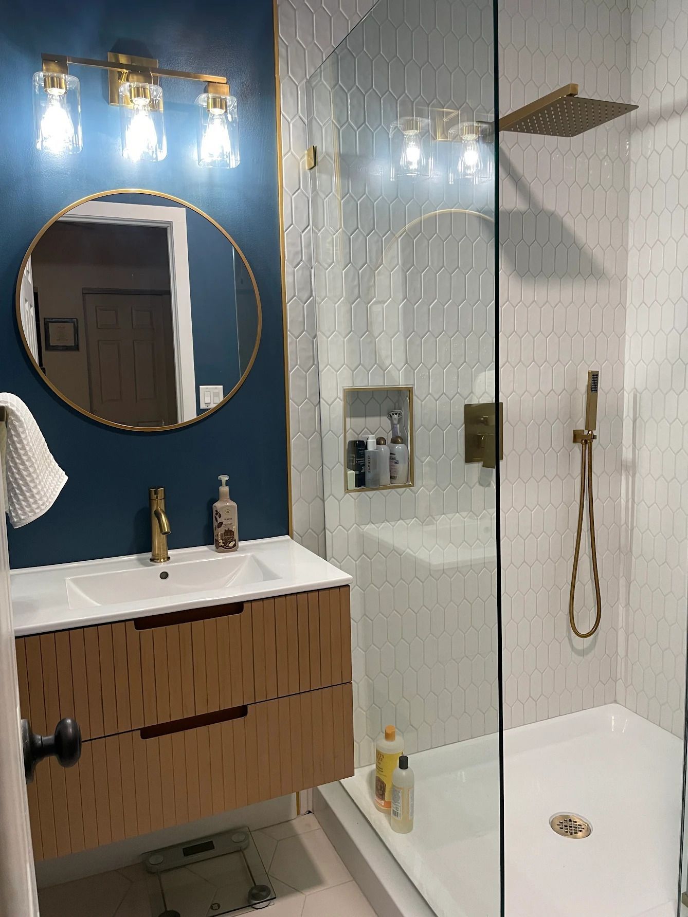 Bathroom with blue walls, round mirror, wood vanity, glass shower, and built-in white bathtub.
