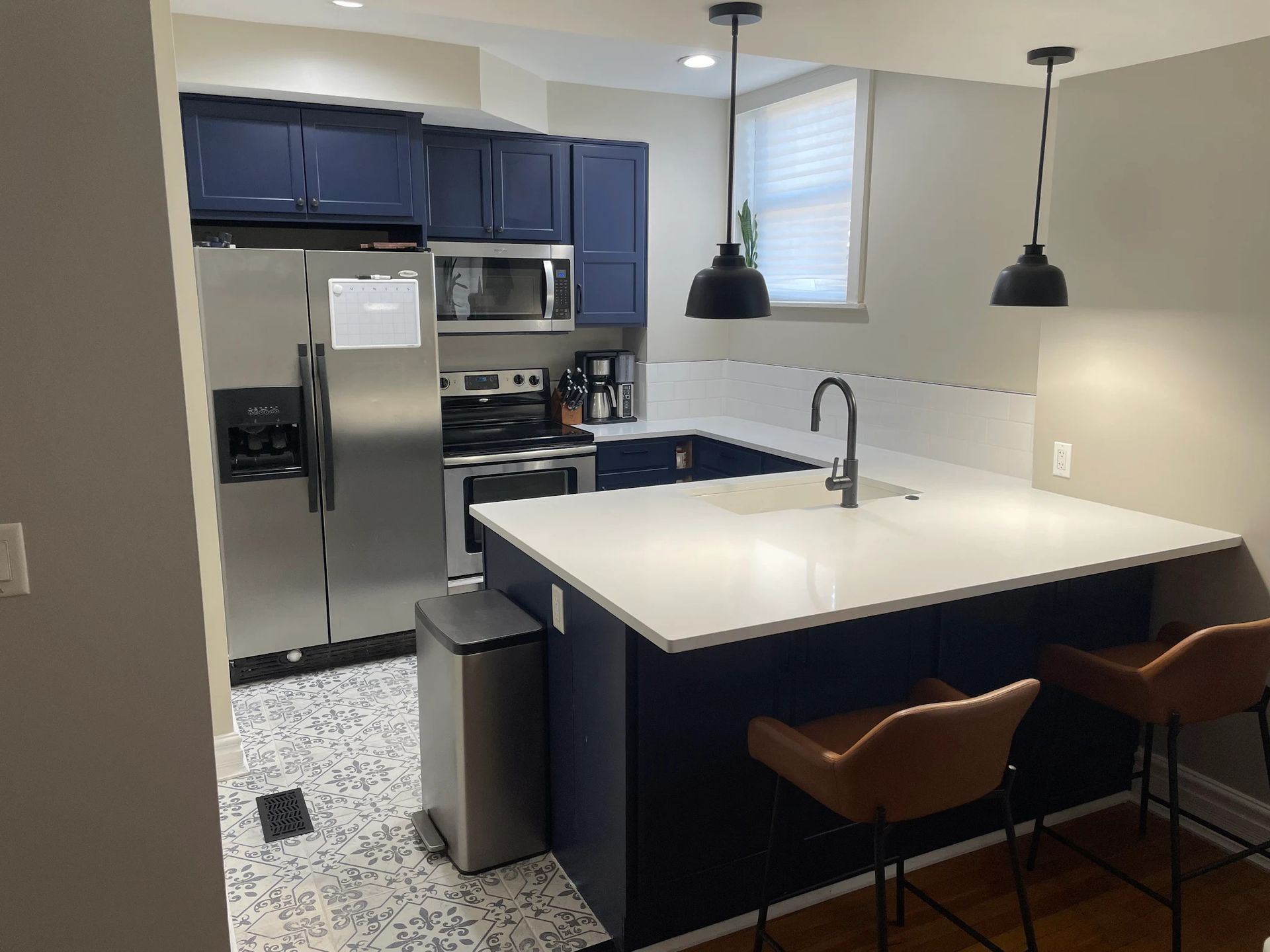 Modern kitchen with blue cabinets, stainless fridge, white island, and two brown stools
