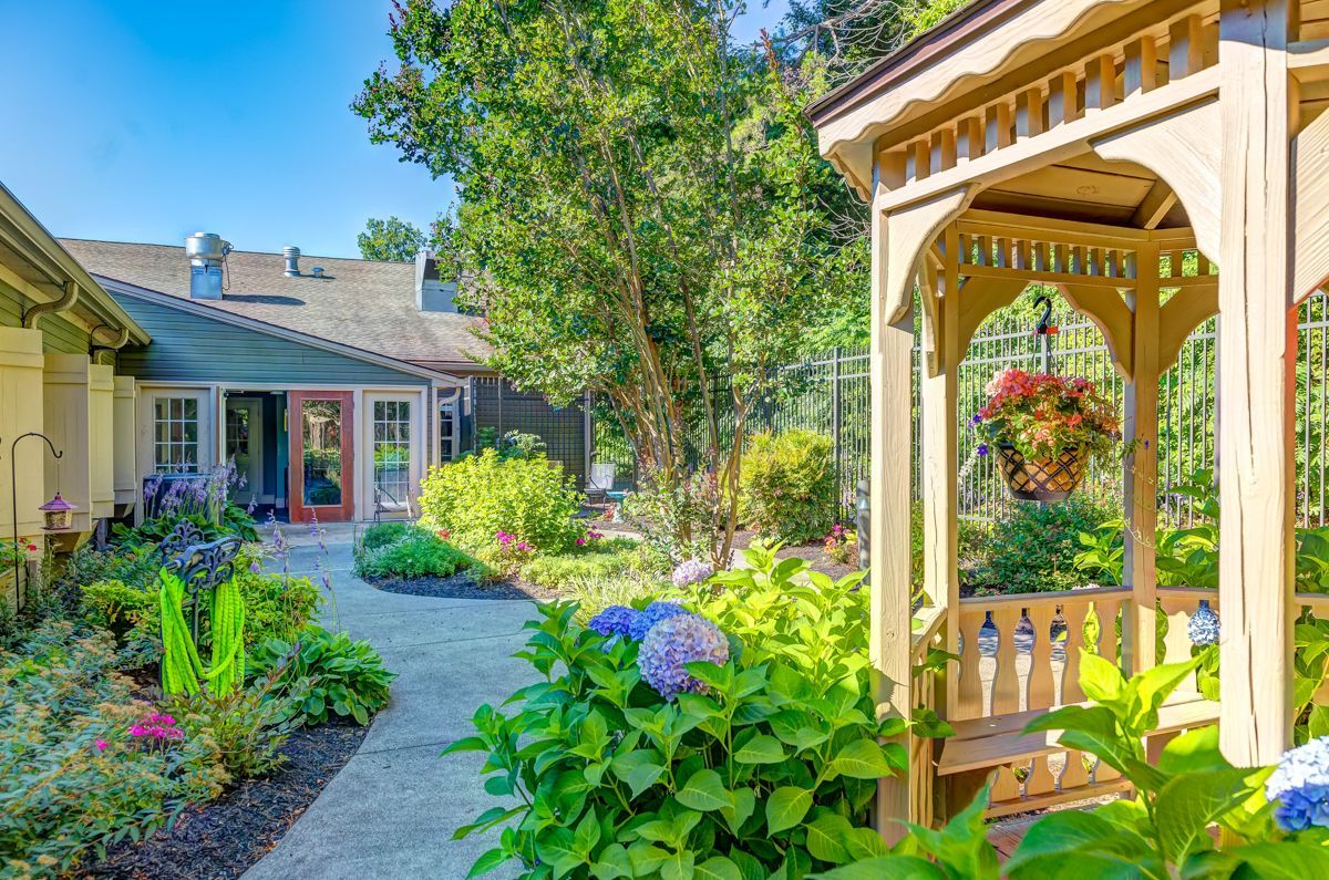 There is a gazebo in the middle of a garden next to a house.
