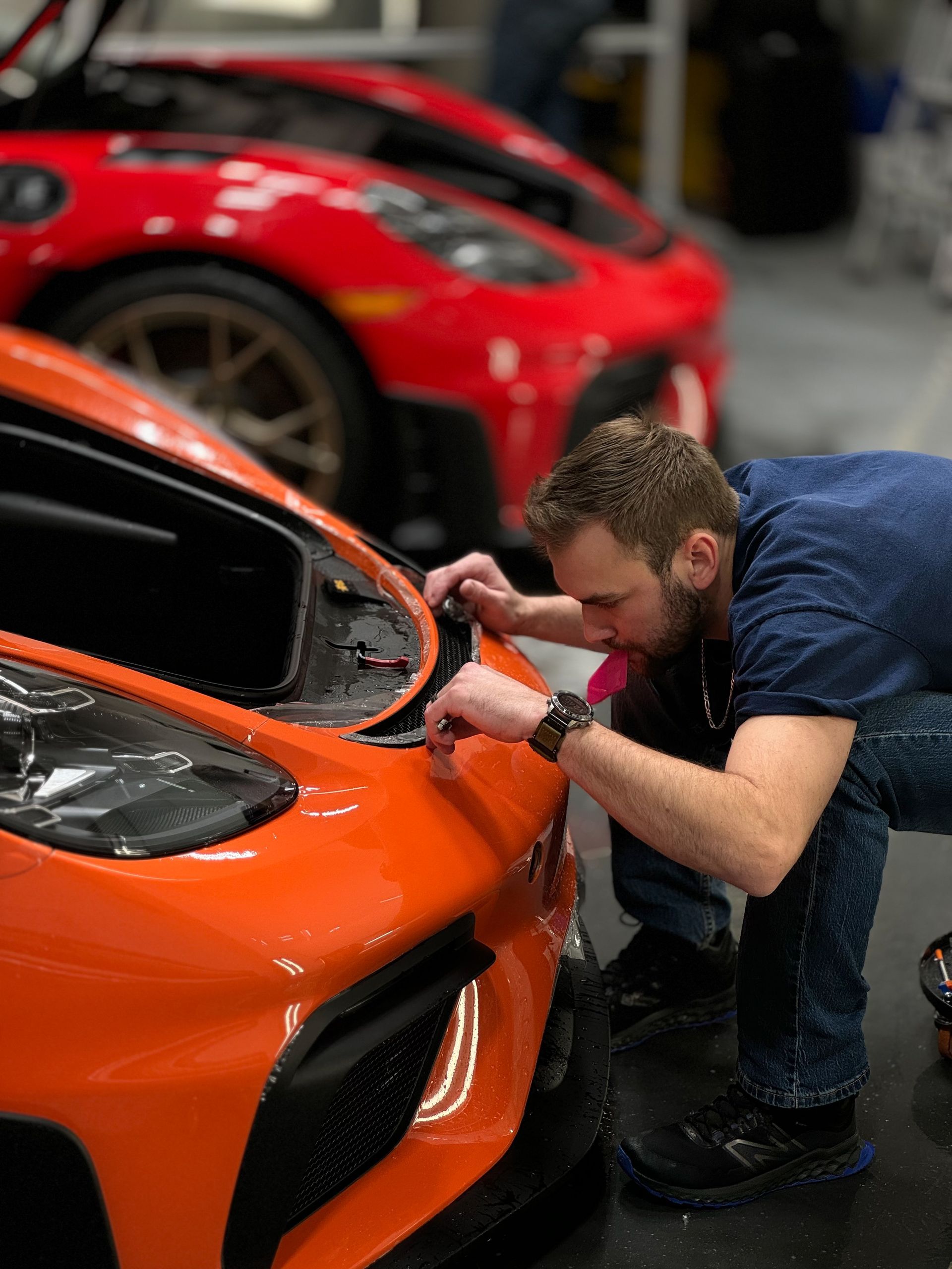 A man is working on the front of an orange sports car.