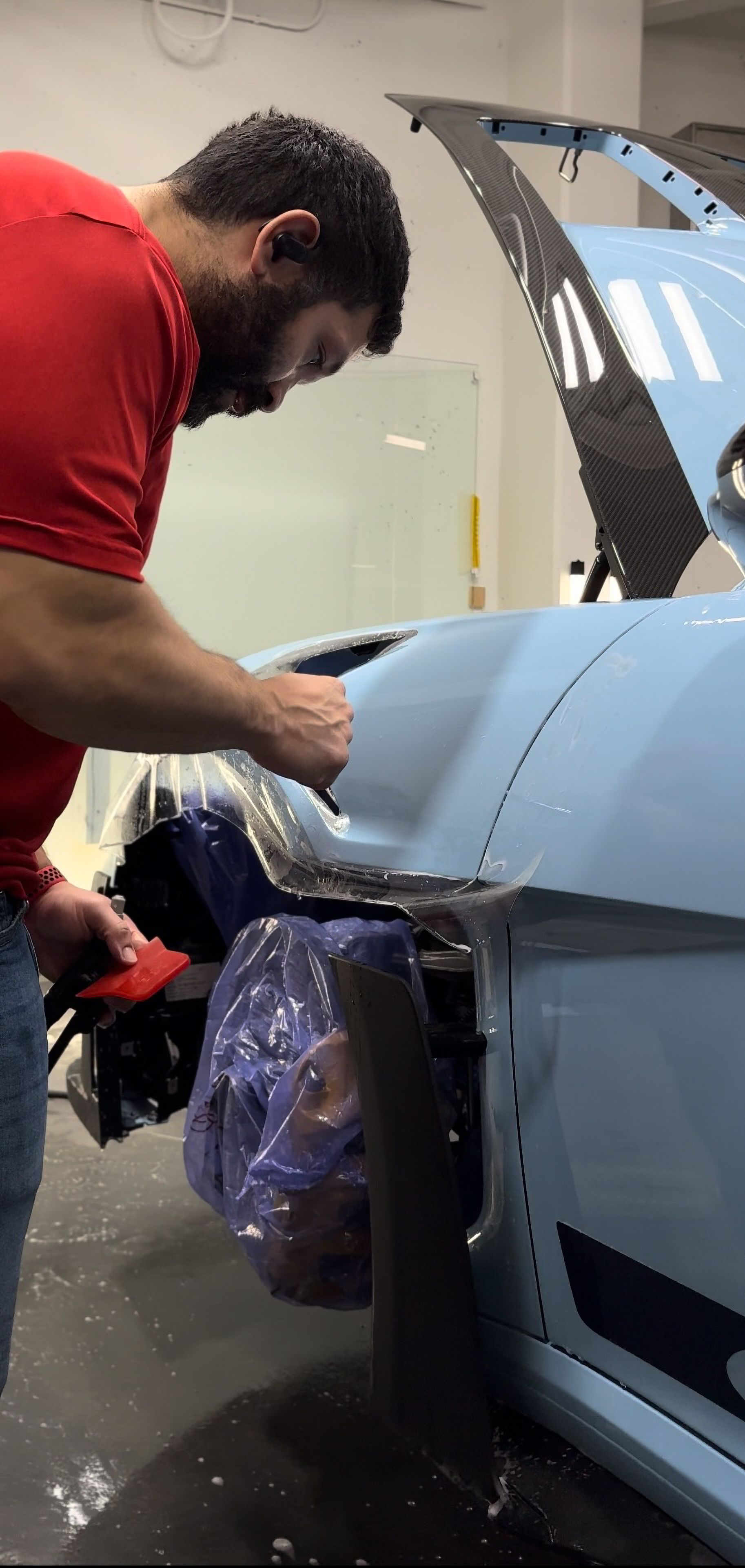A man in a red shirt is working on a blue car.
