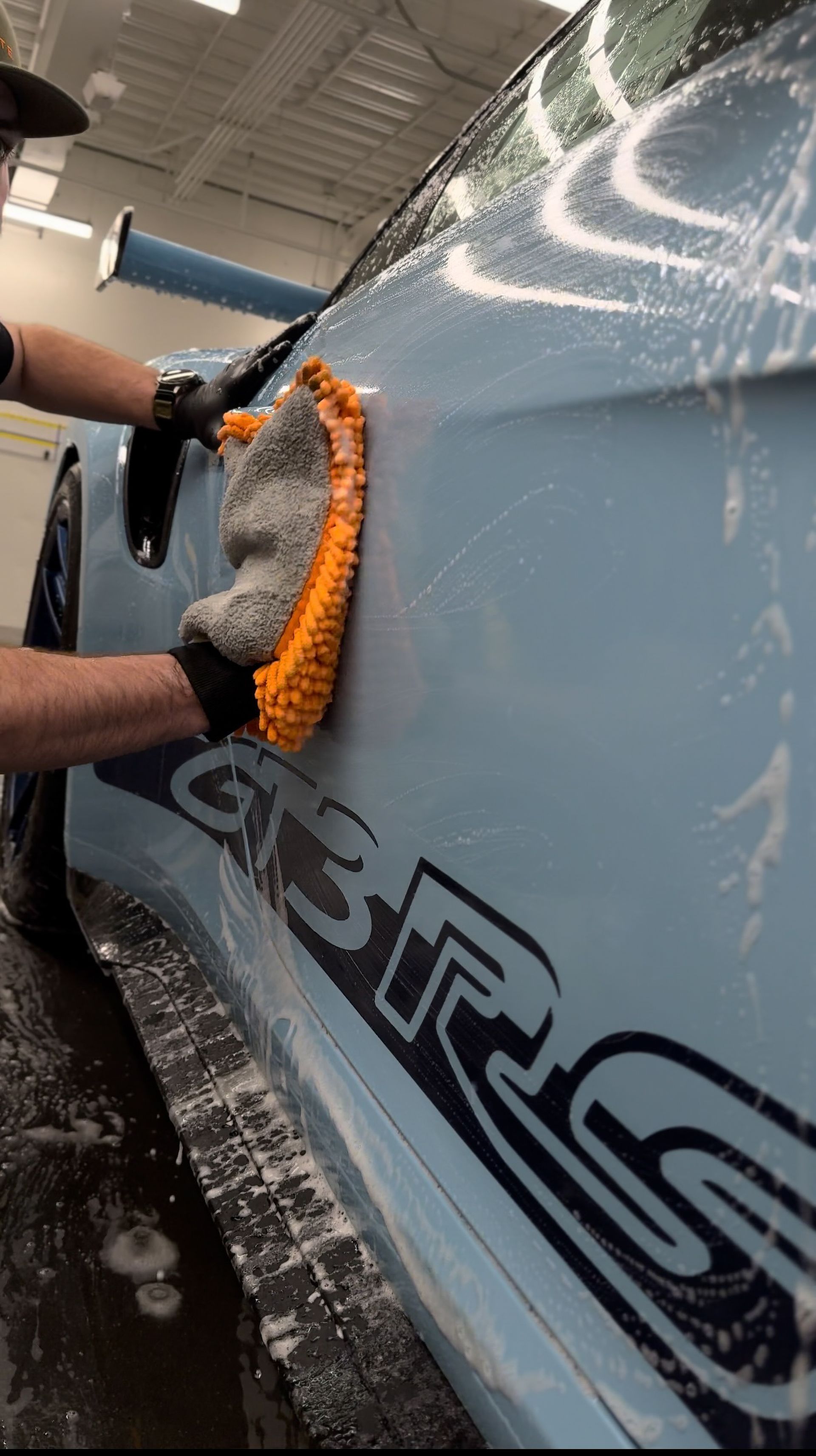 A person is washing a blue car with a towel.