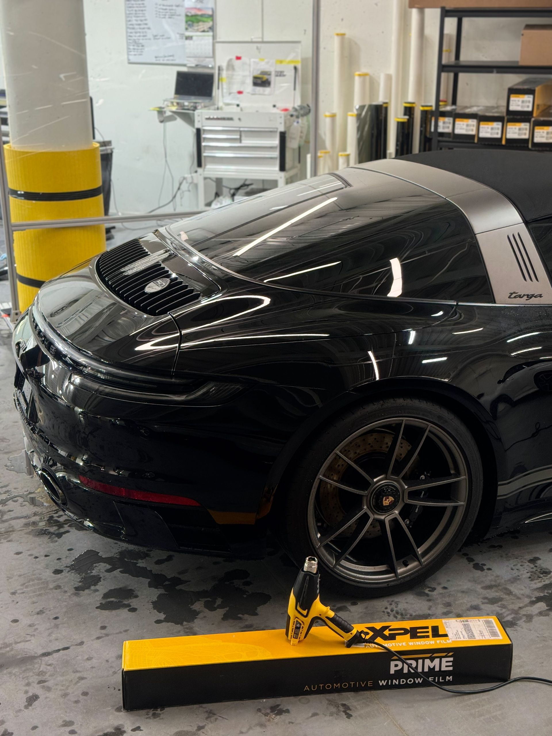 A black porsche 911 targa is sitting in a garage next to a dewalt drill.