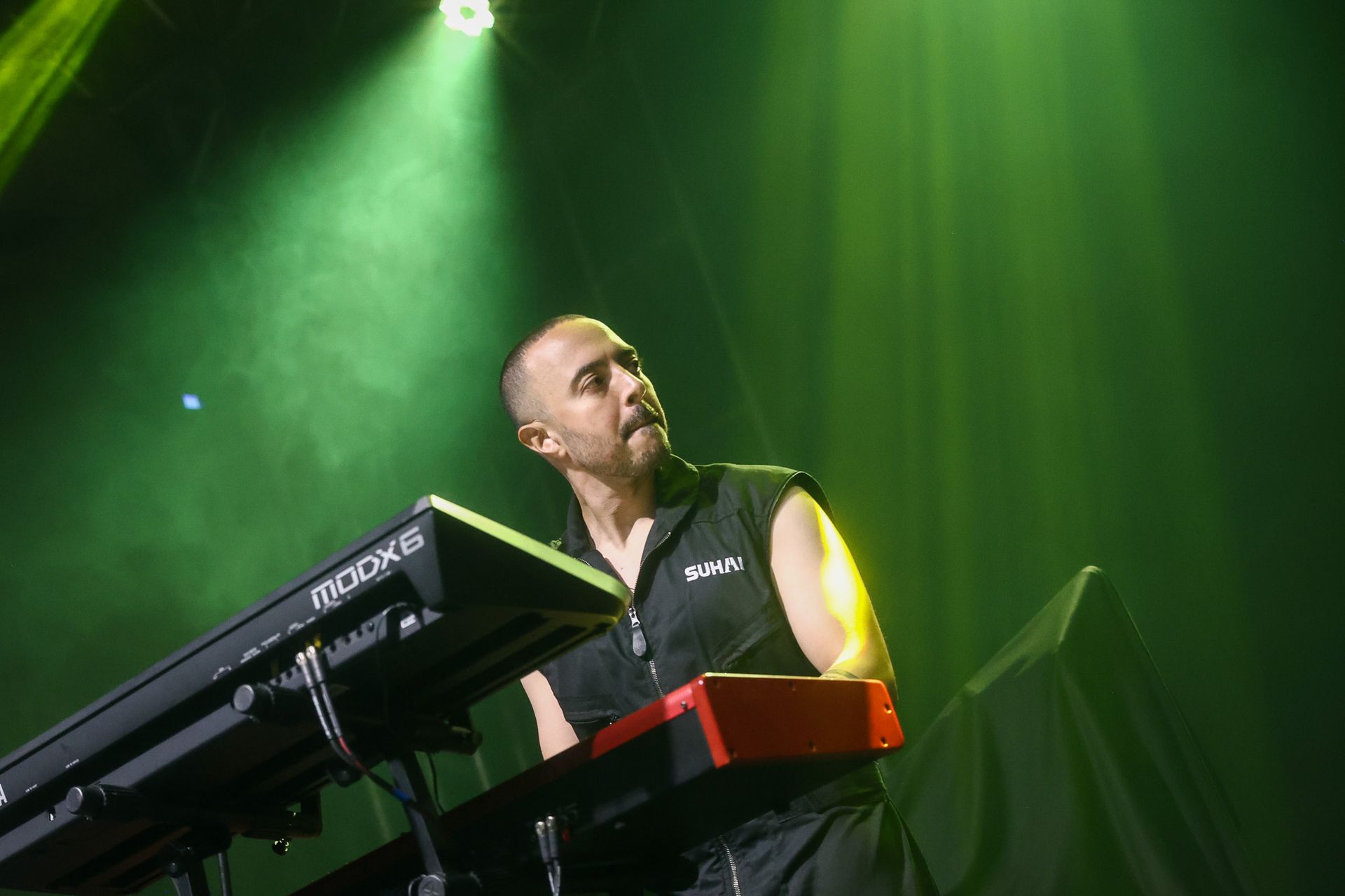 Um músico toca um teclado em um palco banhado por uma luz verde brilhante.