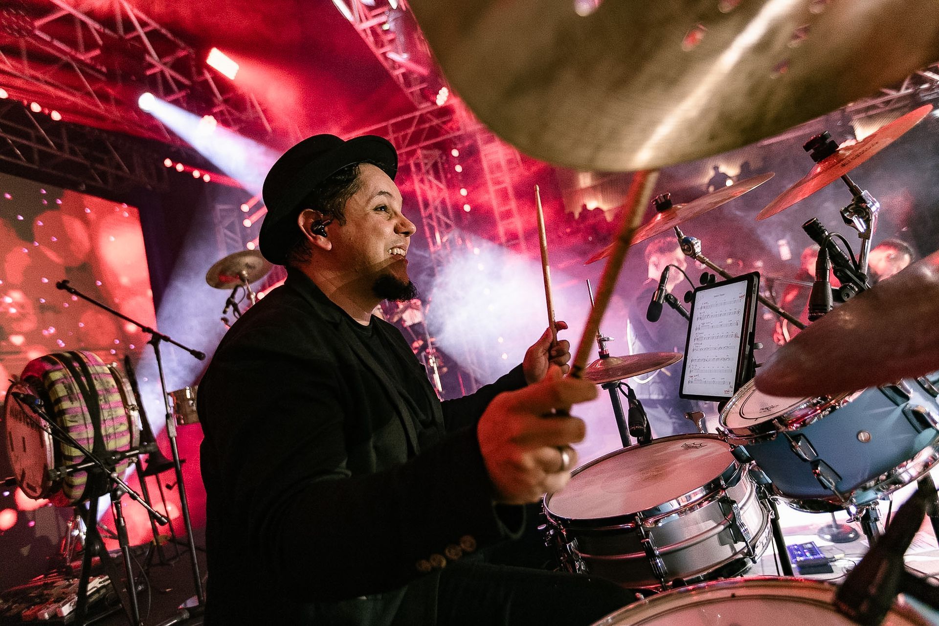 Baterista se apresentando no palco sob luzes vermelhas e roxas, capturado em plena ação atrás de uma bateria.